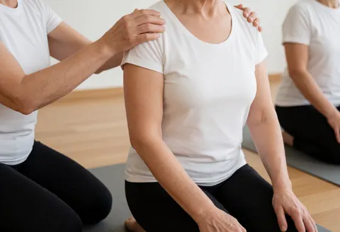 Une instructrice de yoga ajuste la posture de l'épaule d'une élève en position genoux sur tapis dans un studio.