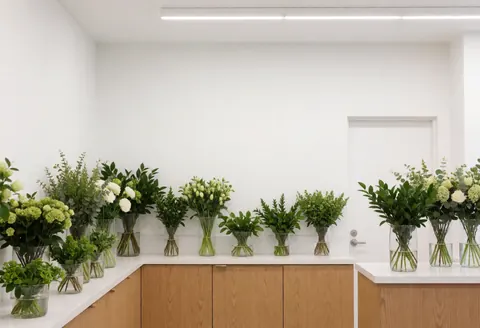 Vue intérieure d'une fleuristerie au style épuré présentant plusieurs bouquets de fleurs fraîches disposés dans des vases en verre sur un comptoir blanc.