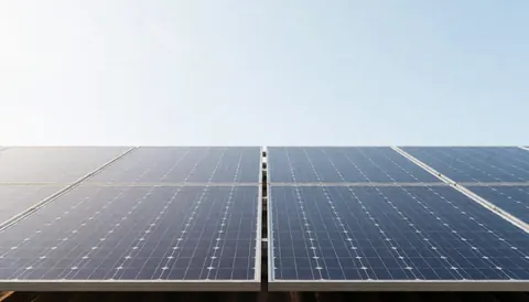 Vue de panneaux photovoltaïques installés sur une toiture avec un fond de ciel bleu dégagé, évoquant l'énergie propre et durable.