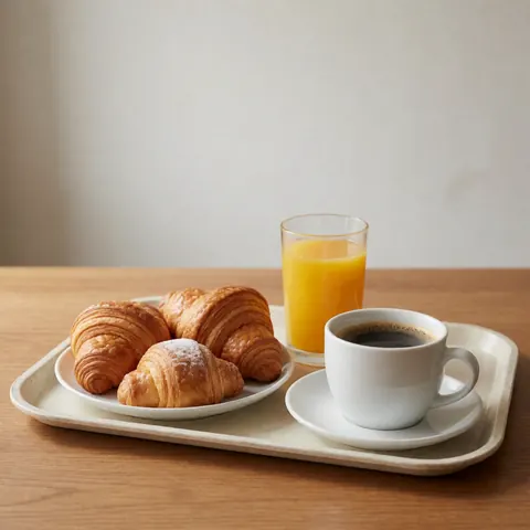 Un plateau posé sur une table en bois contient des croissants, un café noir et un verre de jus d'orange. Vue générale sans personnes.