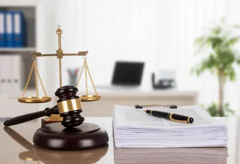 Marteau de juge et balance de justice posés sur un bureau avec des documents et un stylo.
