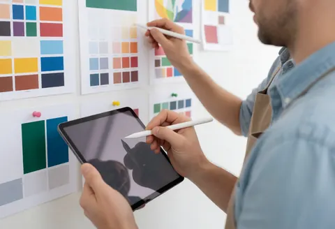 Un homme adulte utilise une tablette et un stylet numérique pour sélectionner des palettes de couleurs sur un mur présentant des échantillons.