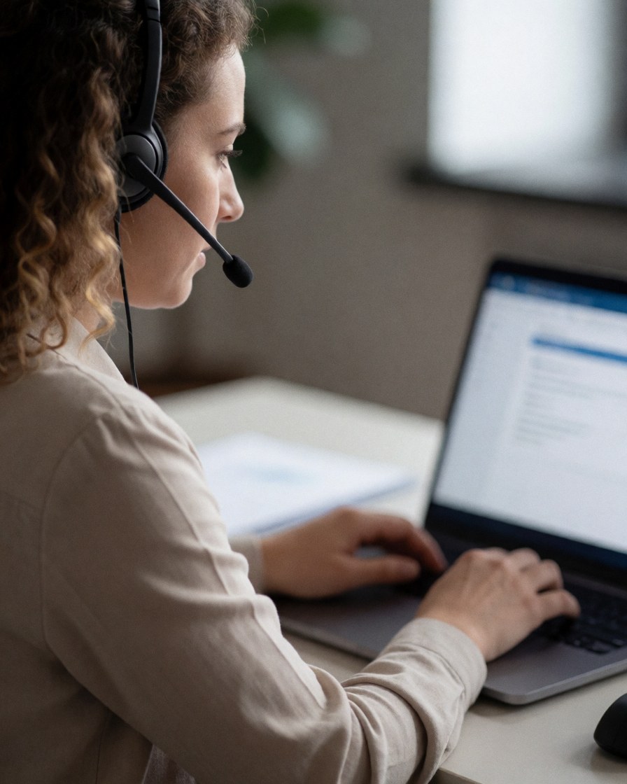 Une femme utilisant un ordinateur et un casque pour gérer une demande de service client dans un environnement de bureau moderne.