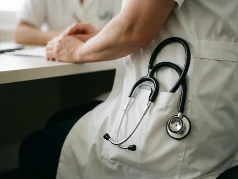 Médecin homme adulte portant une blouse blanche et un stéthoscope, assis dans un bureau médical.