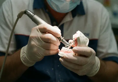 Un dentiste portant des gants et un masque polissant des dents sur un modèle avec un outil électrique.