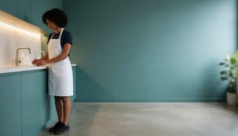 Une esthéticienne en tablier blanc se lave les mains au lavabo d'une clinique moderne aux murs turquoise.