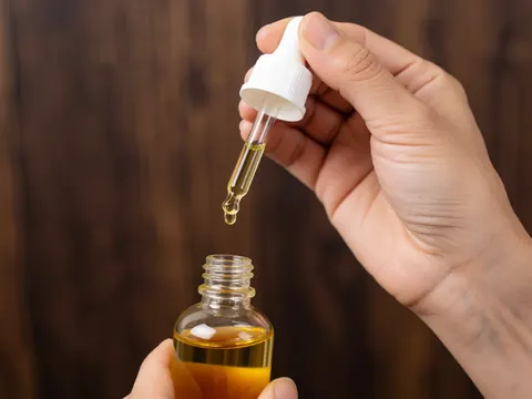 Goutte d'huile d'argan brillante au premier plan, évoquant le soin capillaire et la beauté naturelle.