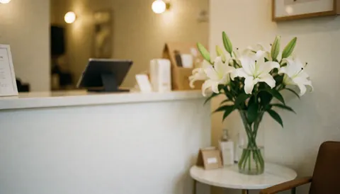 Intérieur chaleureux d'un salon de coiffure montrant une réception avec un vase de lys blancs, une tablette et une chaise, servant de fond pour du texte publicitaire.