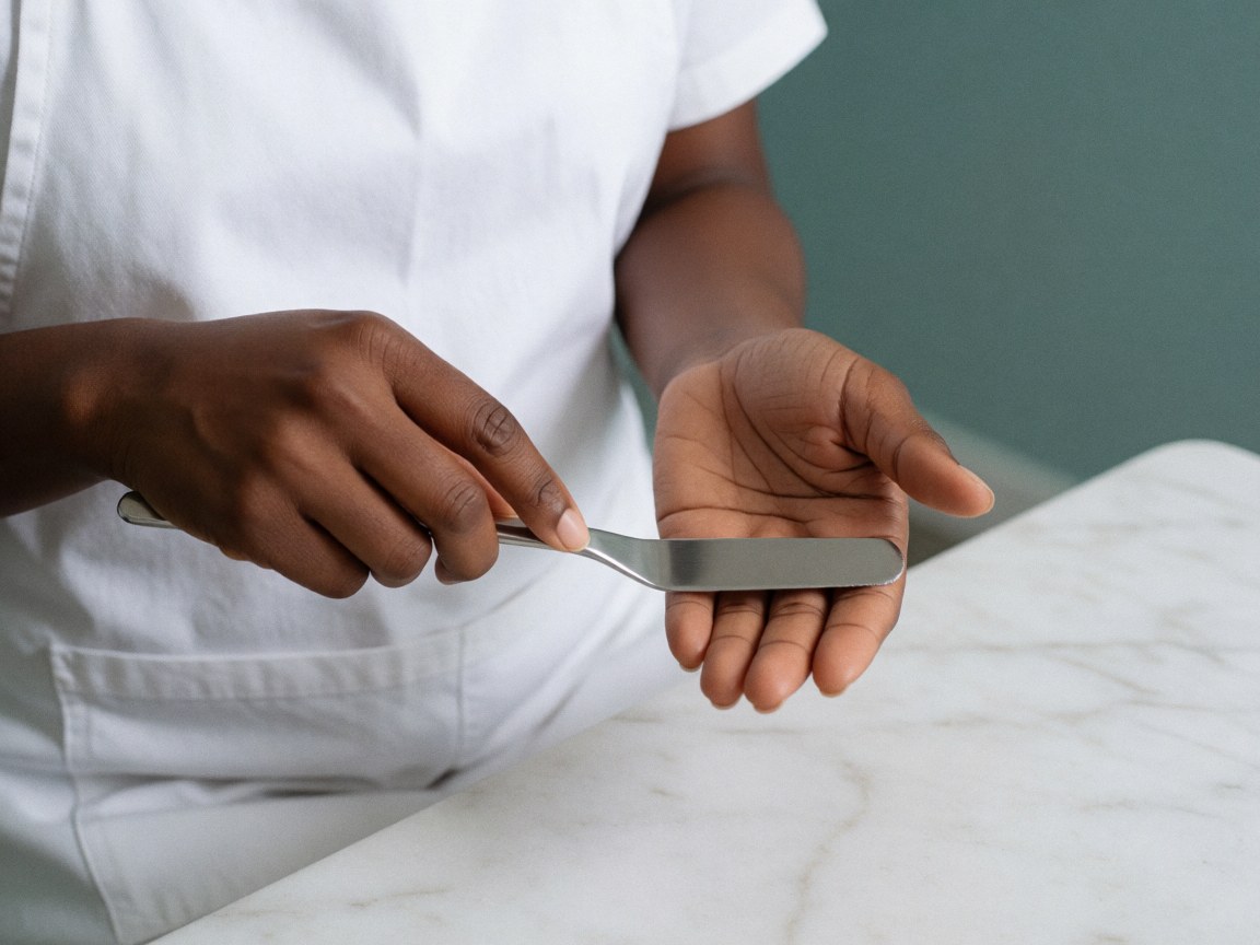 Des mains professionnelles utilisent une spatule pour appliquer du gel sur la paume, dans un cadre esthétique au marbre blanc et aux murs turquoise.