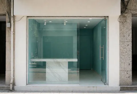 Façade d'une clinique de beauté avec murs bleu-vert, table en marbre et fenêtre en verre. Entrée propre et accueillante, idéale pour les entreprises de beauté.