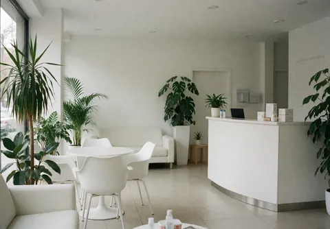 Réception moderne de clinique dentaire avec meubles blancs, plantes vertes et un environnement propre et accueillant pour les patients.