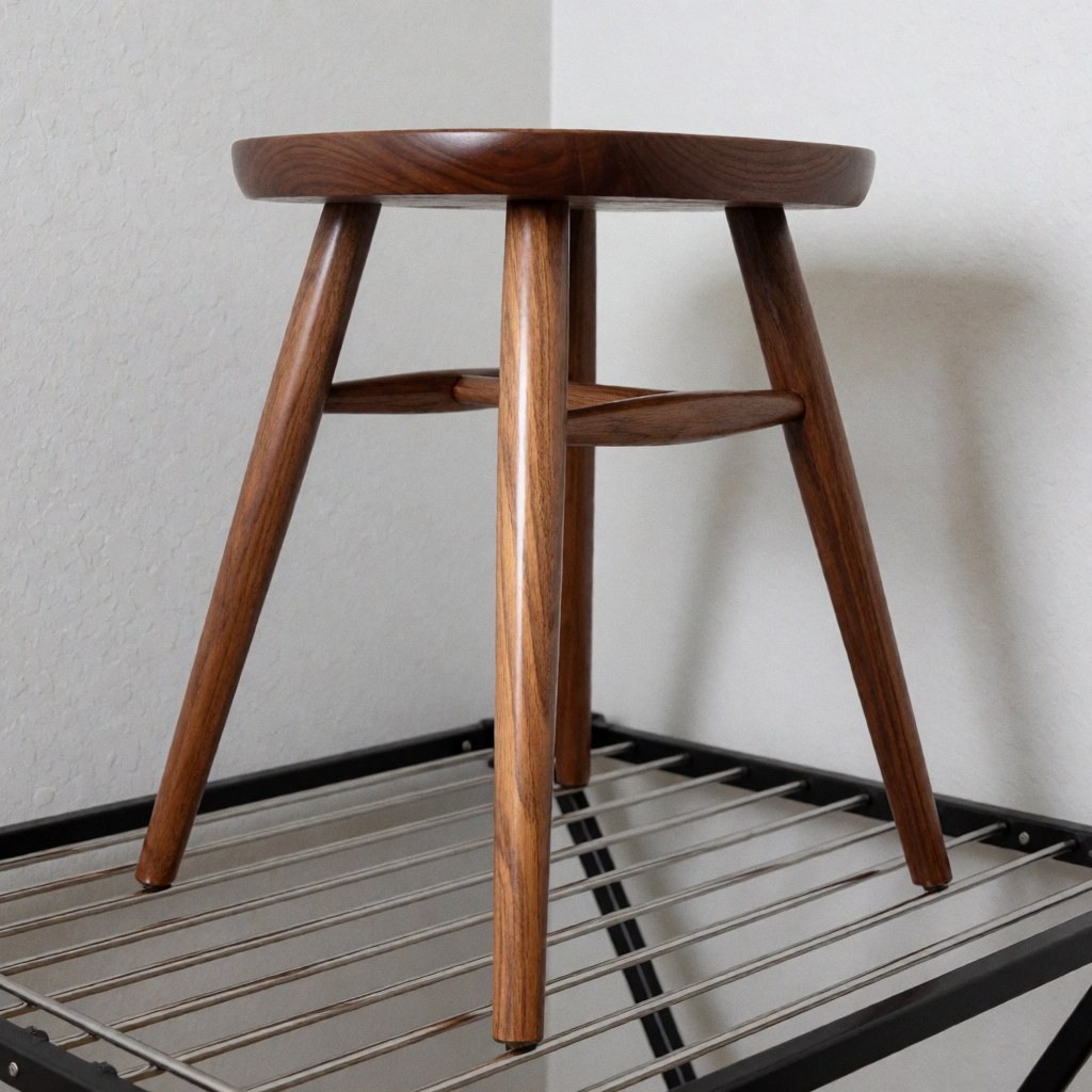 Chaise en bois restaurée avec une finition brillante, pieds visibles posés sur un étagère métallique, fond de murs gris clair et éclairage professionnel.