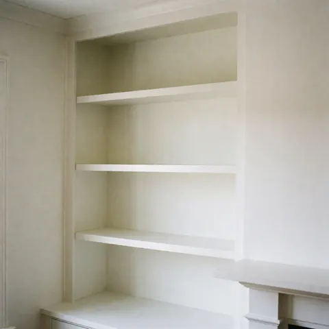 Meuble blanc encastré avec trois étagères vides, murs blancs, éclairage naturel, finition polie, idéal pour montrer des services de design intérieur.