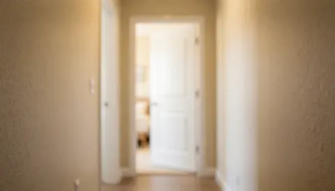 Couloir de maison aux murs texturés et une porte blanche entrouverte, éclairé par une lumière chaude, idéal comme arrière-plan pour des textes sur les services de sécurité ou de réparation.