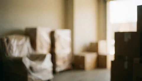 Arrière-plan flou d'un entrepôt contenant des cartons et des meubles enveloppés, éclairé par une lumière chaude, idéal pour textes commerciaux et services logistiques.