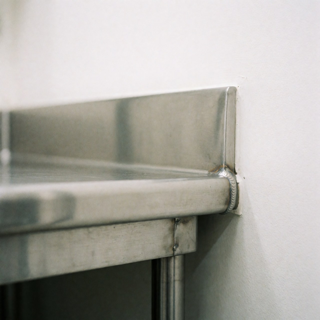 Bord d'acier inoxydable poli avec soudure visible sur fond blanc, surface propre et brillante pour cuisines professionnelles.