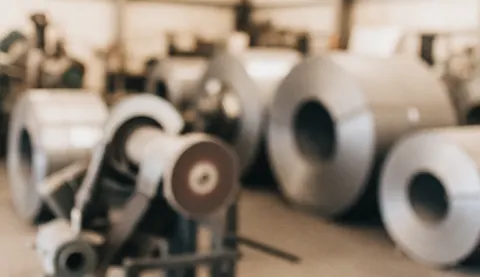Arrière-plan flou d'une usine d'acier montrant des bobines métalliques et des outils industriels, servant de support visuel pour l'intégration de texte commercial.