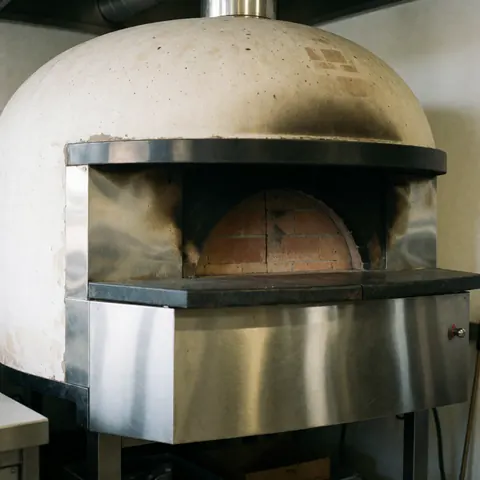 Four à bois compact de couleur sombre avec une porte en métal, conçu pour la cuisson professionnelle dans une cuisine commerciale.