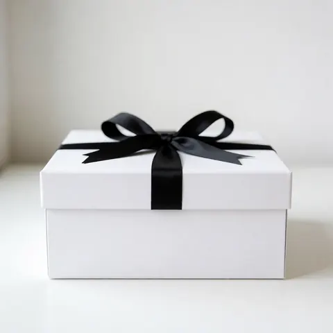 Une boîte cadeau blanche fermée ornée d'un ruban noir noué en nœud, présentée sur un fond uni pour un rendu élégant et minimaliste.