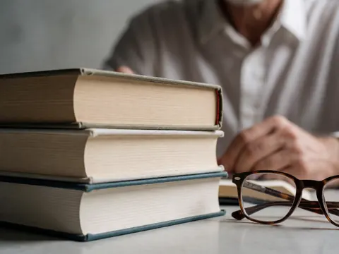 Pile de livres reliés avec des lunettes de lecture posées sur un bureau en béton, évoquant un environnement intellectuel et professionnel.