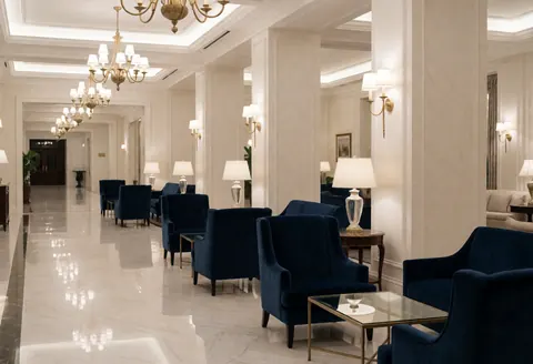 Lobby d'hôtel vide au sol en marbre blanc, fauteuils bleus, lustres dorés et murs blancs. Ambiance élégante et raffinée.