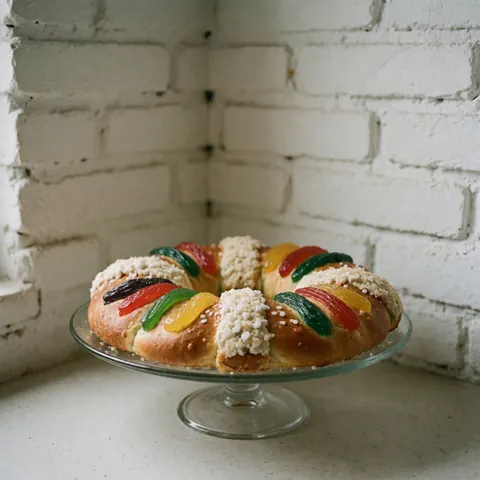 Gâteau en couronne décoré de fruits confits colorés posé sur une vitrine en verre devant un mur de briques.