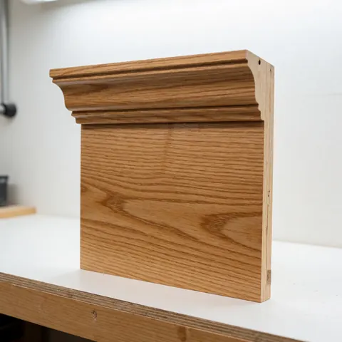 Détail d'une moulure de couronnement en bois massif, montrant le grain et la finition lisse du matériau.