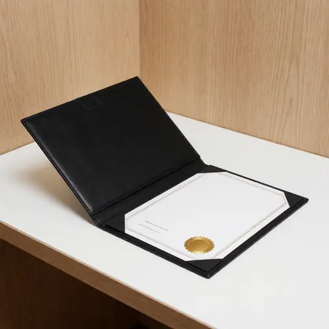 Un portefeuille professionnel noir posé sur un bureau blanc, accompagné d'un certificat officiel avec sceau doré, évoquant la réussite et le travail.