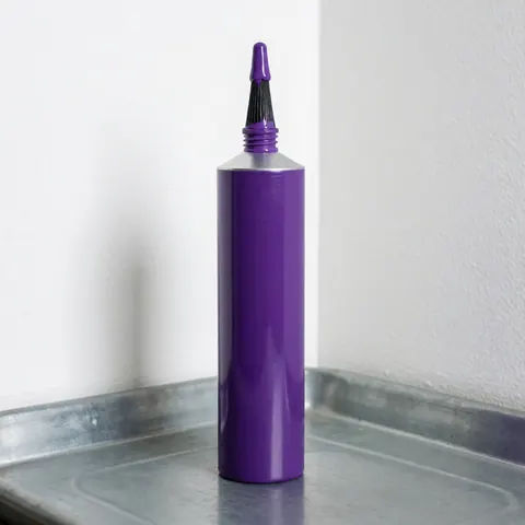 Un tube de colle pour PVC violet posé à côté d'un pinceau applicateur et d'une bande métallique sur une surface blanche, éclairage studio.