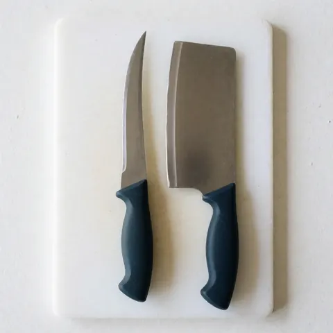 Couteau désosseur et couteau de découpe posés sur une planche à découper en bois, outils professionnels de cuisine commerciale.