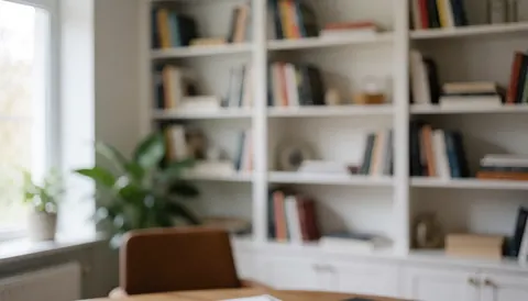 Arrière-plan d'espace de travail moderne comprenant une étagère blanche, des livres, une plante verte et une fenêtre offrant une lumière naturelle.
