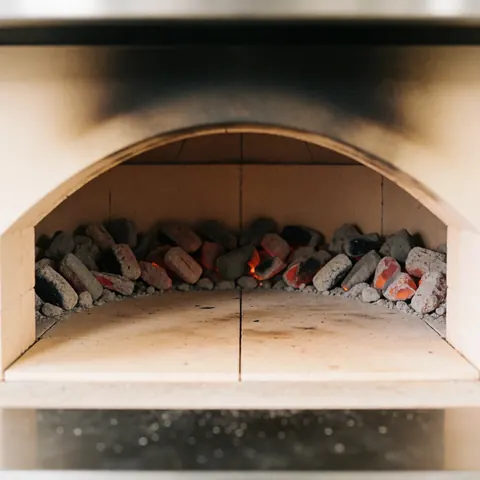 Vue intérieure d'un four de pizza professionnel au feu de bois avec pierres réfractaires et flammes visibles pour la cuisson.