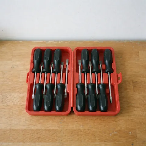 Ensemble de tournevis à manche noir rangés dans une boîte ouverte posée sur un banc de travail en bois, éclairage naturel et scène professionnelle.