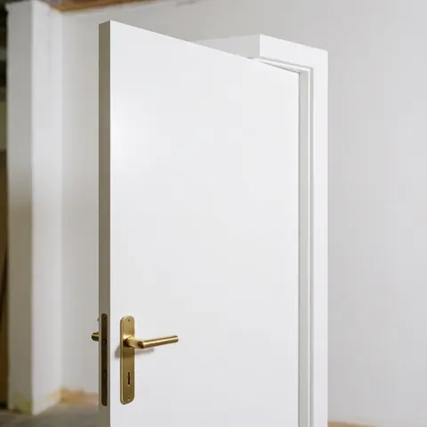 Une porte intérieure moderne en bois peint en blanc, équipée d'une poignée de couleur bronze poli, vue de face dans un environnement clair.