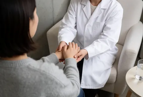 Un thérapeute en blouse blanche guide les mains d'un client assis pour un exercice de respiration, dans un cadre professionnel et chaleureux.