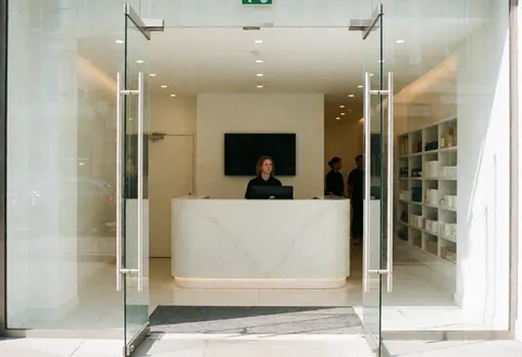 Entrée de gymnase moderne avec réception, vitres, tables et design minimaliste. Espace propre, éclairé et professionnel pour petites entreprises.