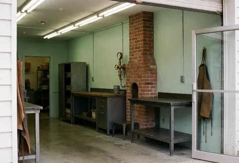 Vue extérieure d'un atelier industriel montrant une façade en briques et une cheminée, typique des bâtiments de production.