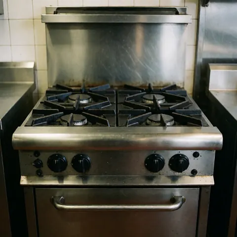Un réchaud à gaz professionnel en acier inoxydable avec plusieurs brûleurs, installé dans une cuisine commerciale aux murs carrelés.