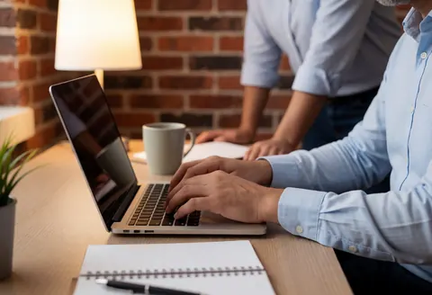 Scène professionnelle et productive avec ordinateur, mur de briques, lumière chaleureuse, tasse et carnet sur le bureau.