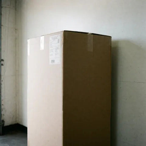 Caisse en carton avec étiquette et code-barres, prête pour le transport, dans un entrepôt aux murs blancs et à la lumière naturelle.