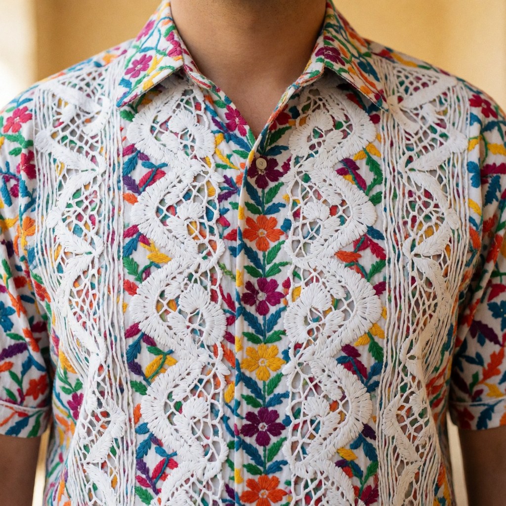 Chemise guayabera aux broderies colorées et à la dentelle blanche, coupe courte, idéale pour des portraits professionnels dans un contexte latino-américain sur fond chaud flou.