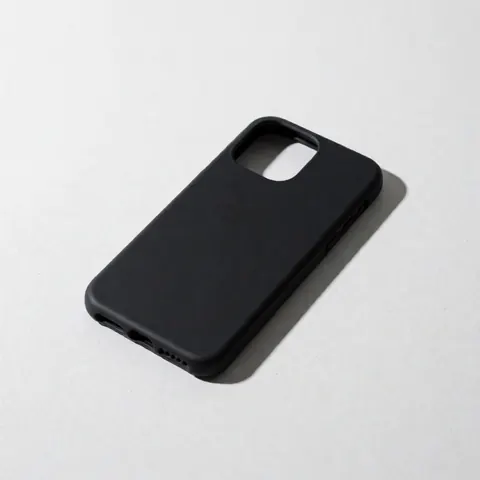 Étui de smartphone noir mat posé sur une surface en béton blanc avec éclairage froid précis et ombre définie à droite, esthétique minimaliste moderne.