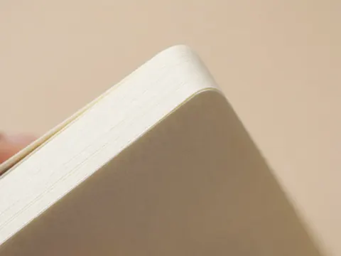 Vue rapprochée montrant la texture du papier épais et les bords d'un carnet de notes posé sur un bureau, évoquant le travail et l'organisation professionnelle.