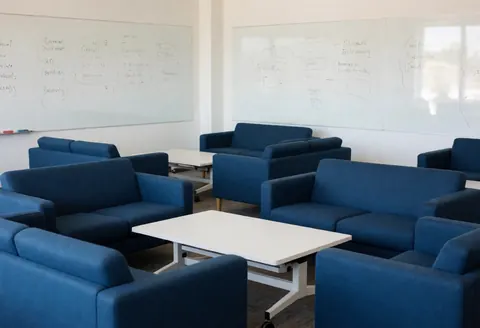 Salle de réunion moderne équipée de canapés bleus, de tables blanches et de tableaux blancs illustrant des schémas, créant une ambiance détendue et propice au travail d'équipe.