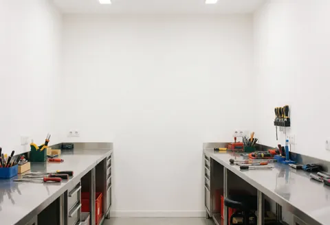 Espace de travail propre avec plans de travail en acier inoxydable, outils rangés et murs blancs, éclairage lumineux et ambiance professionnelle.