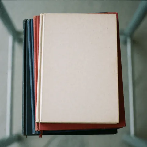 Vue de dessus d'une pile de livres aux couvertures colorées posée sur une surface en verre avec un éclairage uniforme, symbolisant l'éducation et le savoir.