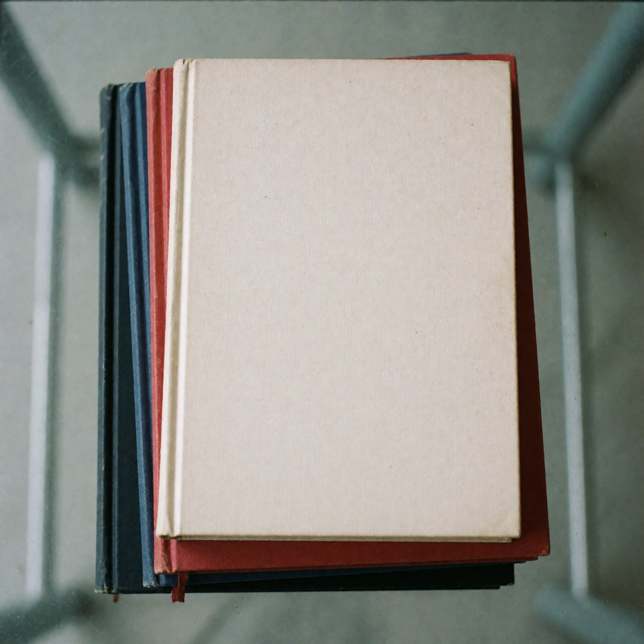 Vue de dessus d'une pile de livres aux couvertures colorées posée sur une surface en verre avec un éclairage uniforme, symbolisant l'éducation et le savoir.