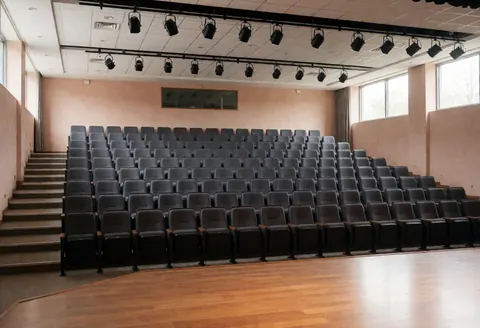 Vue intérieure d'un auditorium universitaire désert montrant des rangées de sièges vides face à une grande scène éclairée, idéale pour conférences et événements.
