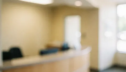 Intérieur flou d'un bureau d'admission avec murs beiges, comptoir et éclairage chaud, idéal pour textes professionnels.