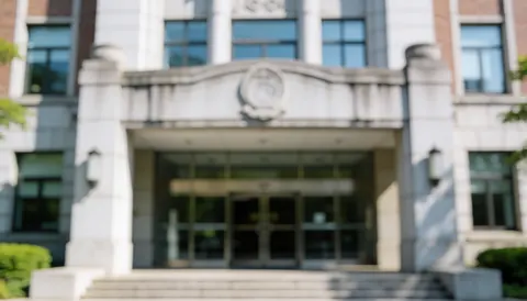 Vue frontale d'une façade en pierre grise et blanche d'un institut de l'enseignement supérieur, montrant des portes, des fenêtres, des escaliers et une architecture professionnelle sur un fond flou.